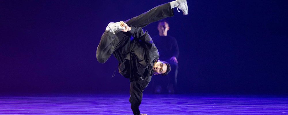 A dancer dressed in all black balances in a one-handed handstand