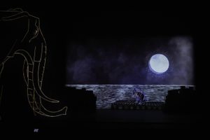 A projection of an elephant and a woman kneeling on a deck in the moonlight