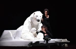 A stage with a large polar bear figure sitting on an iceberg-like structure. A smaller polar bear accompanies it, and there are two puppeteers dressed in black nearby.
