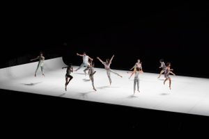 A group of ten contemporary dancers performing on a white stage