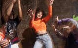 A blurry image of five people in bright clothes dancing against a rocky background. There is a feeling of joy.